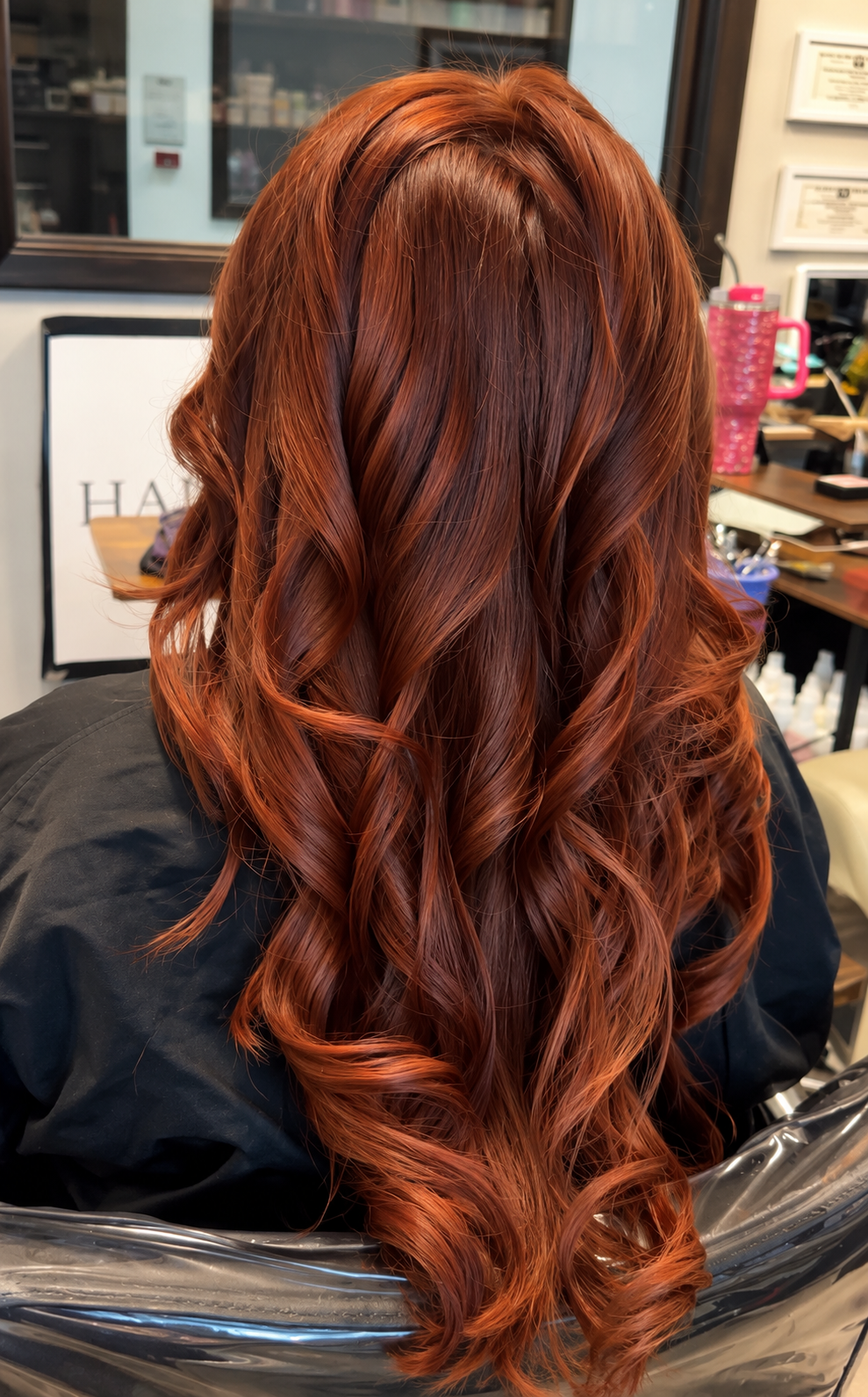 Long wavy copper-red hair styled in loose curls at a salon chair, back view