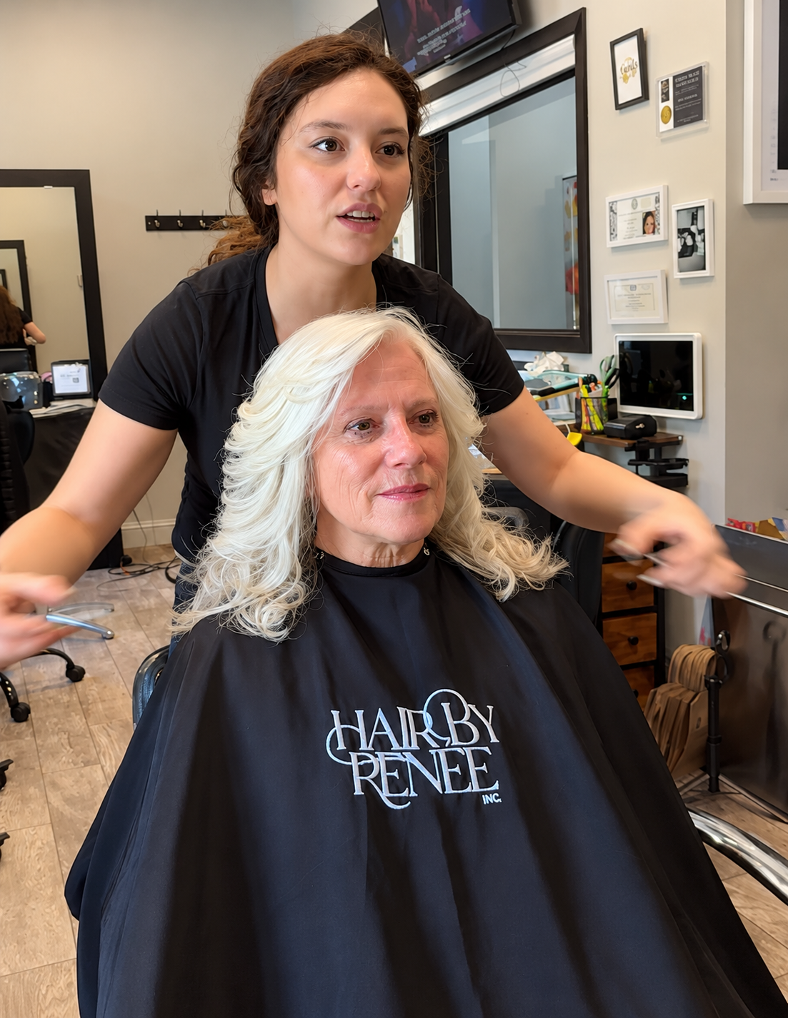 Stylist in black shirt cutting a client’s white hair in a salon chair, cape draped over client.