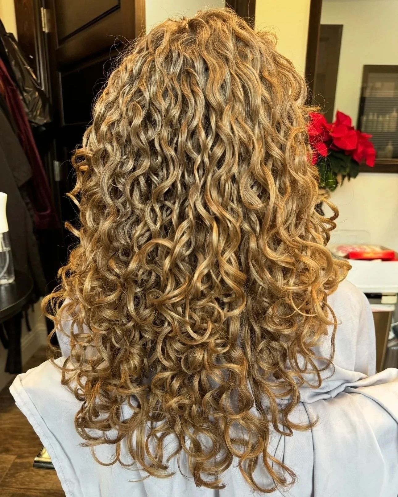 Curly blonde hair styled in loose curls, viewed from behind in a salon chair