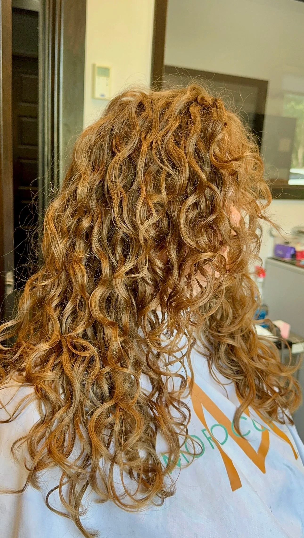 Curly light-brown hair seen from behind in a salon chair indoors