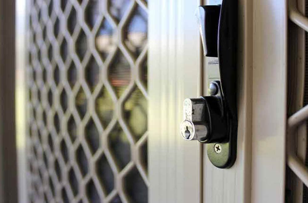 Close-up of a screen door latch on a white door frame with a mesh security screen beside it