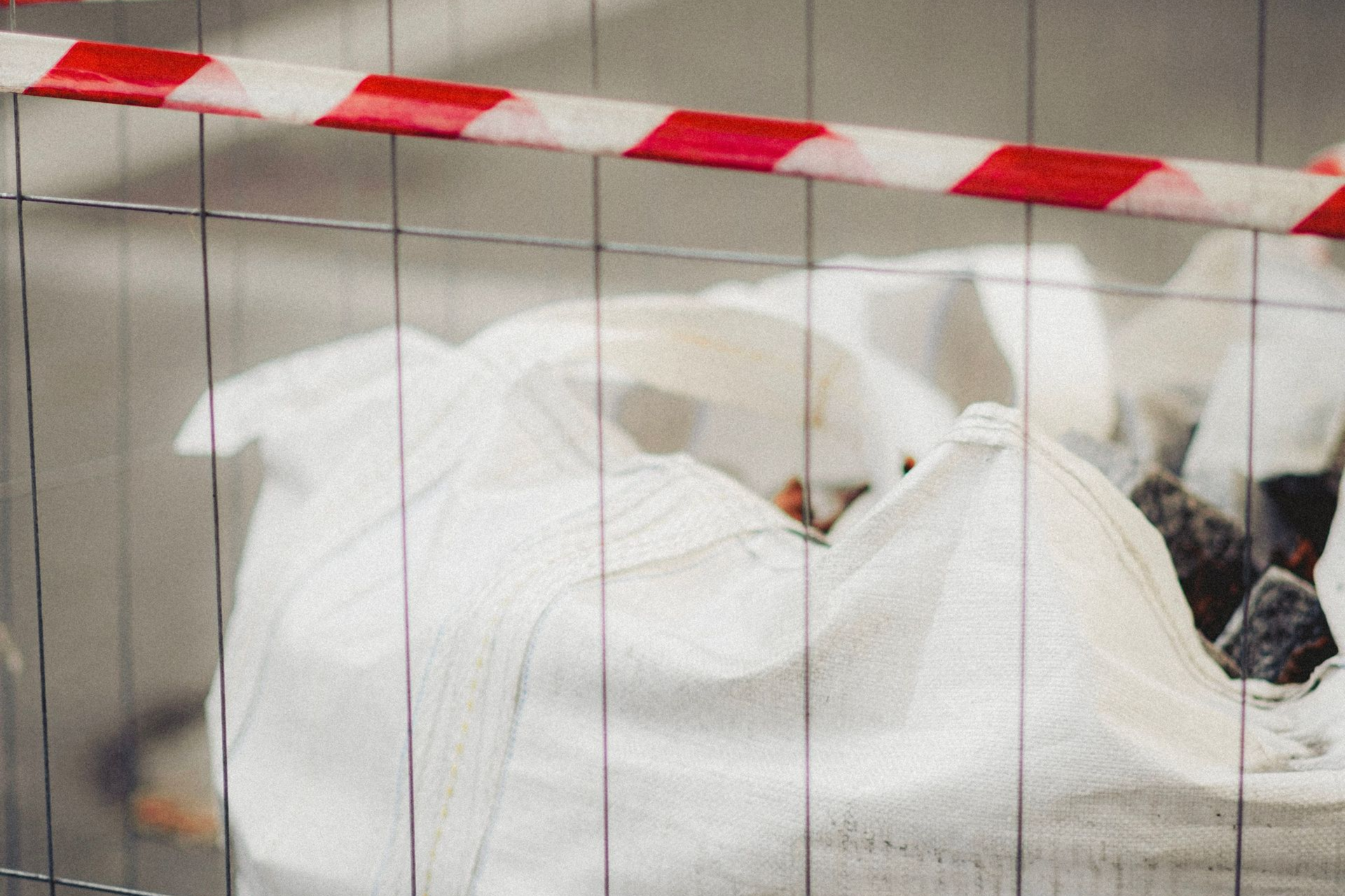 Wrapped white bundles behind red-and-white barrier tape in an industrial setting