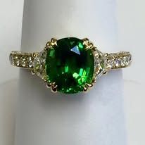 Gold ring with a large, green, round-cut gemstone and smaller diamonds on the band.