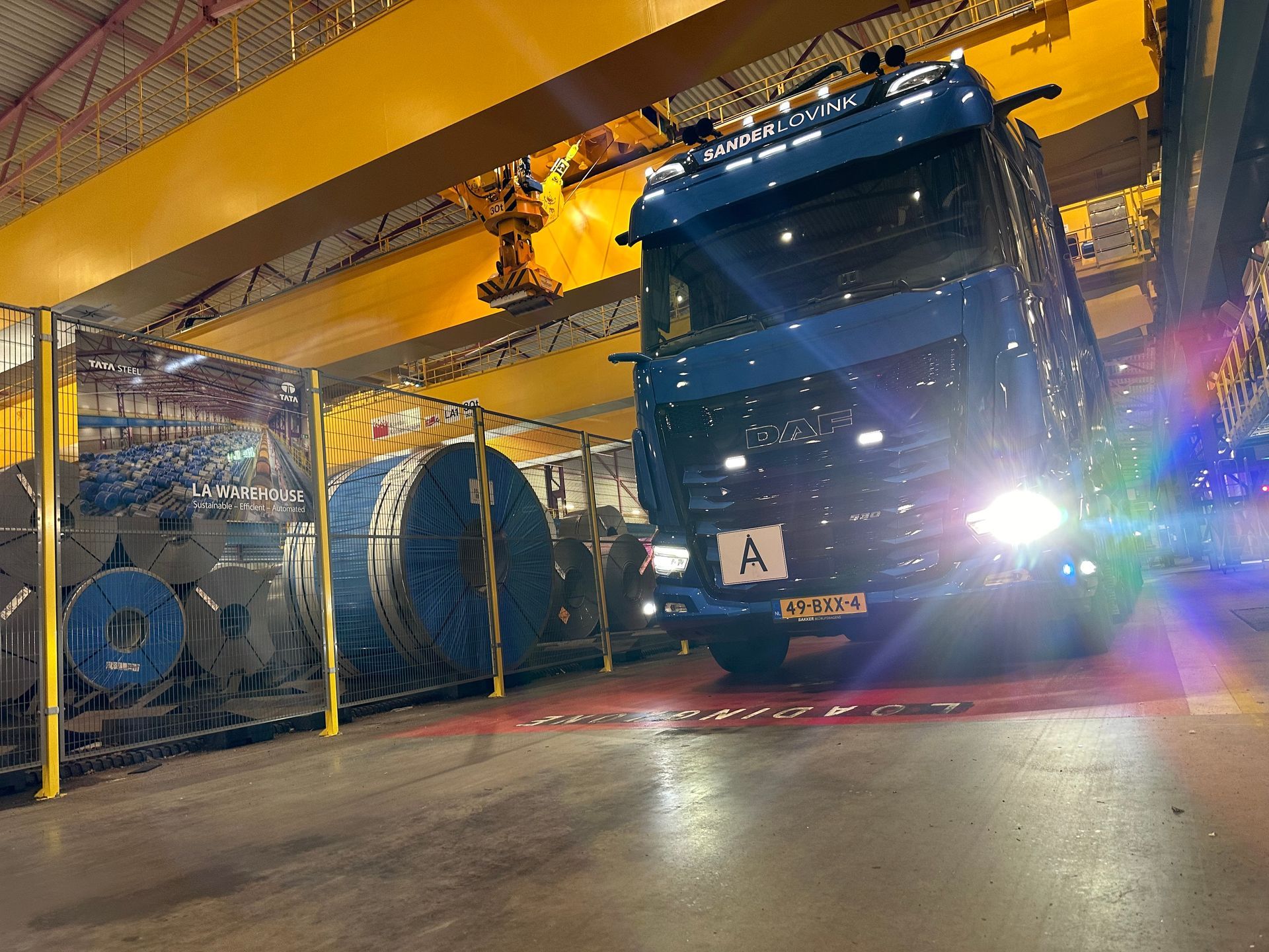 Een blauwe vrachtwagen staat geparkeerd in een felverlichte industriële garage, met grote kabelhaspels in de buurt.
