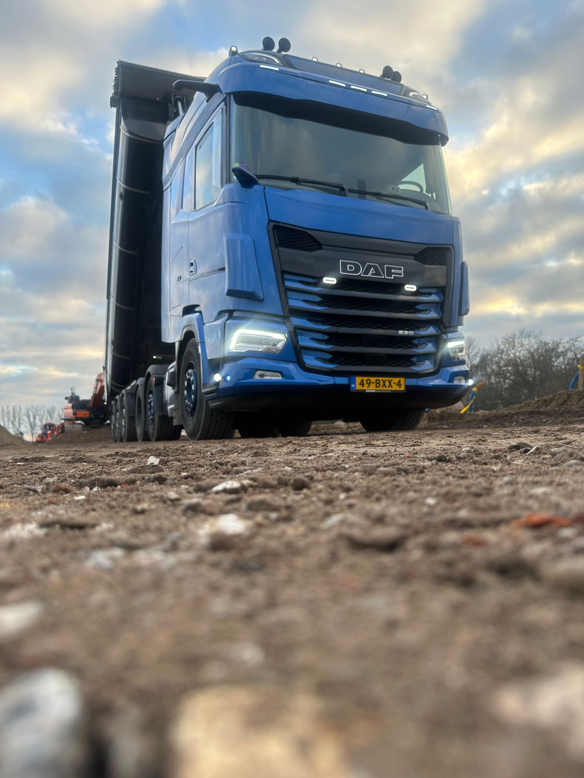 Blauwe vrachtwagen op een modderige weg, laag van voren gefotografeerd onder een bewolkte hemel.