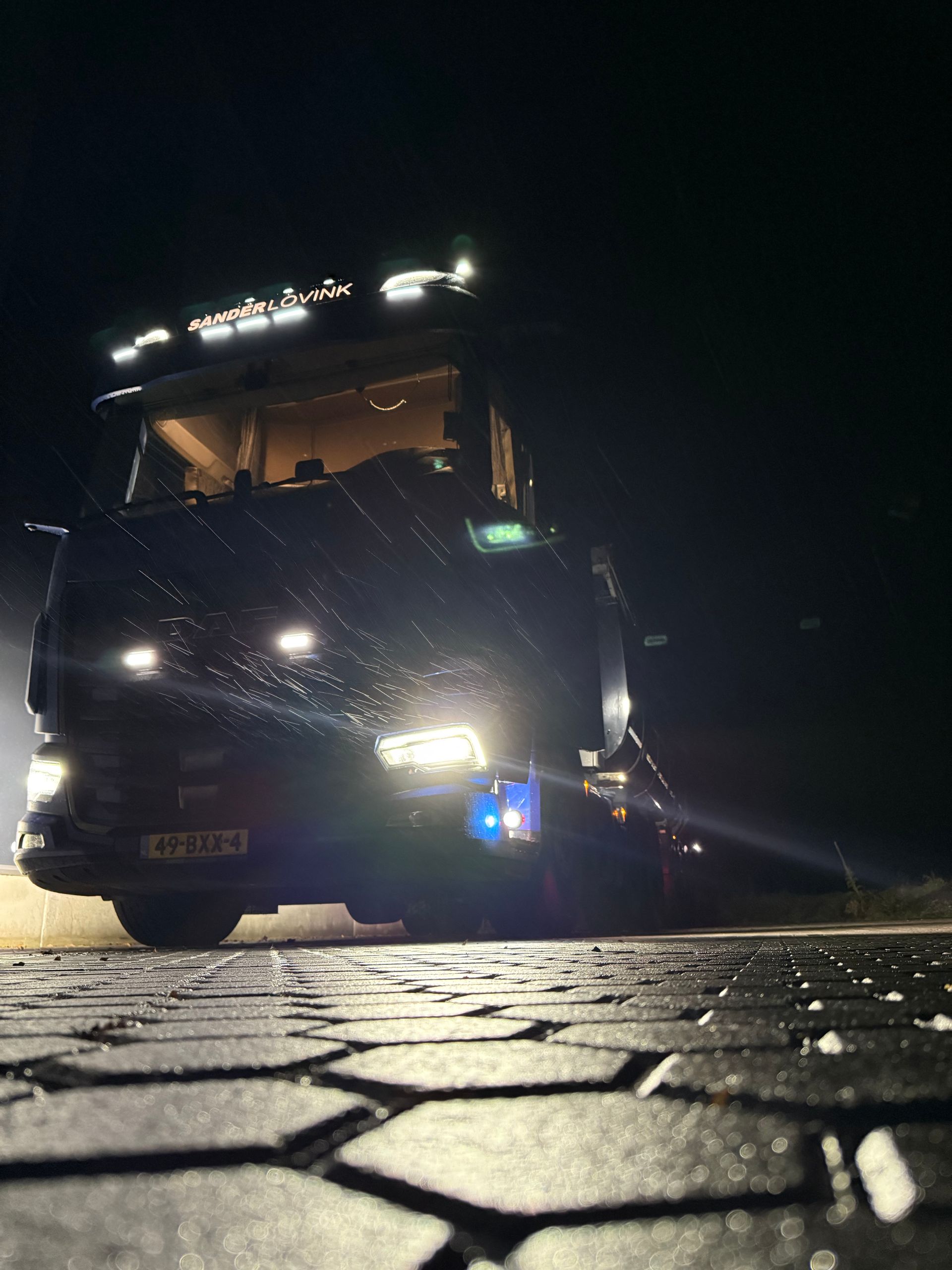 Vrachtwagen met felle koplampen op een straat met kinderkopjes 's nachts