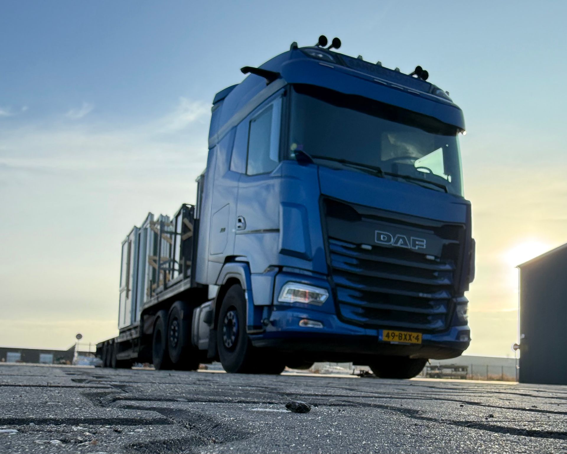 Blauwe vrachtwagen geparkeerd op een verhard terrein bij zonsondergang, vanuit een laag perspectief.