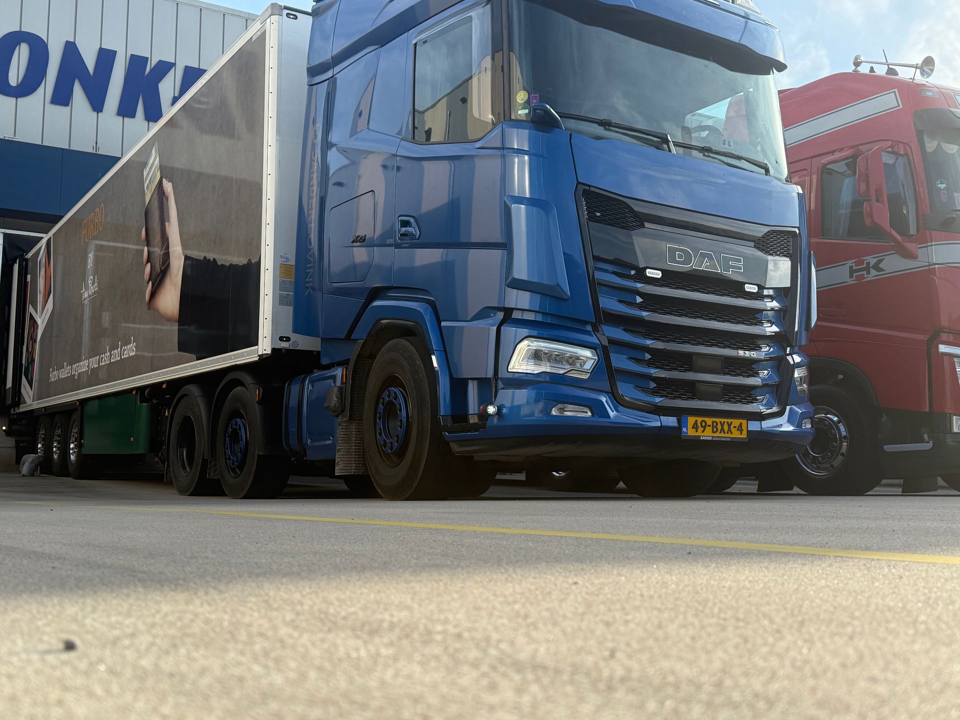 Een blauwe vrachtwagen staat geparkeerd naast een rode vrachtwagen op een industrieterrein.