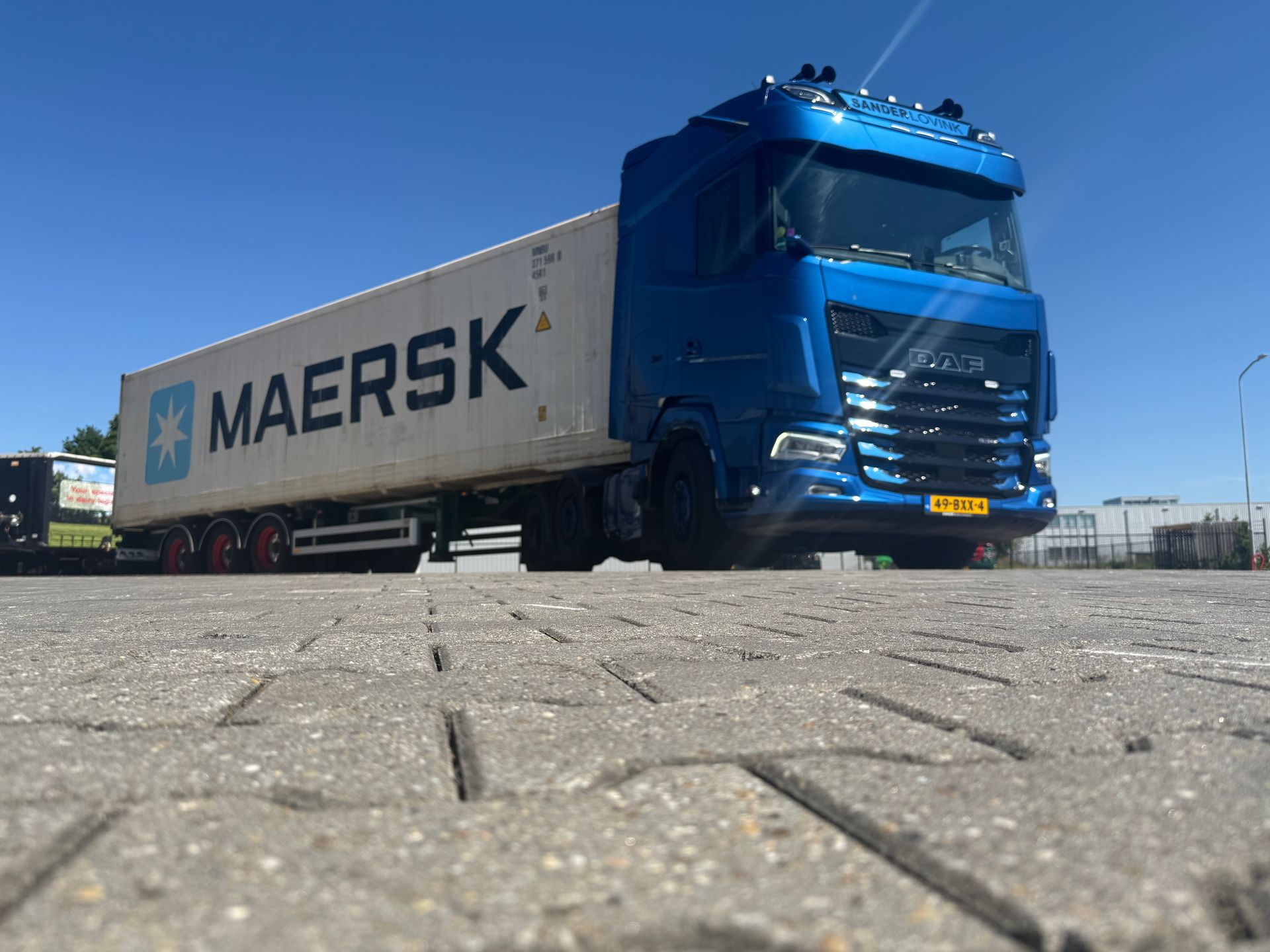 Een blauwe Maersk-vrachtwagen staat geparkeerd op een verhard terrein onder een heldere hemel.