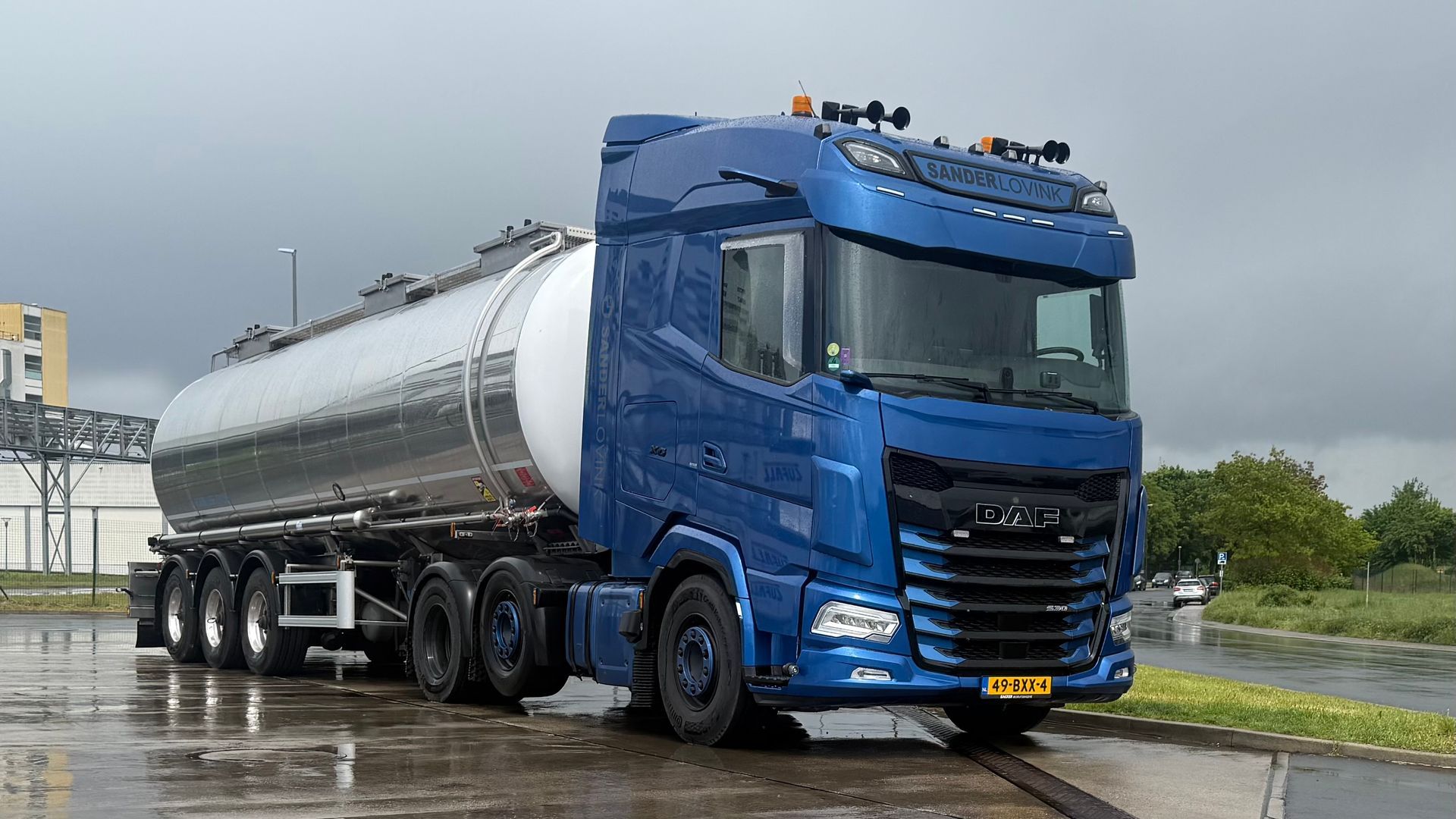 Een blauwe tankwagen staat geparkeerd langs een natte weg onder een grijze hemel.