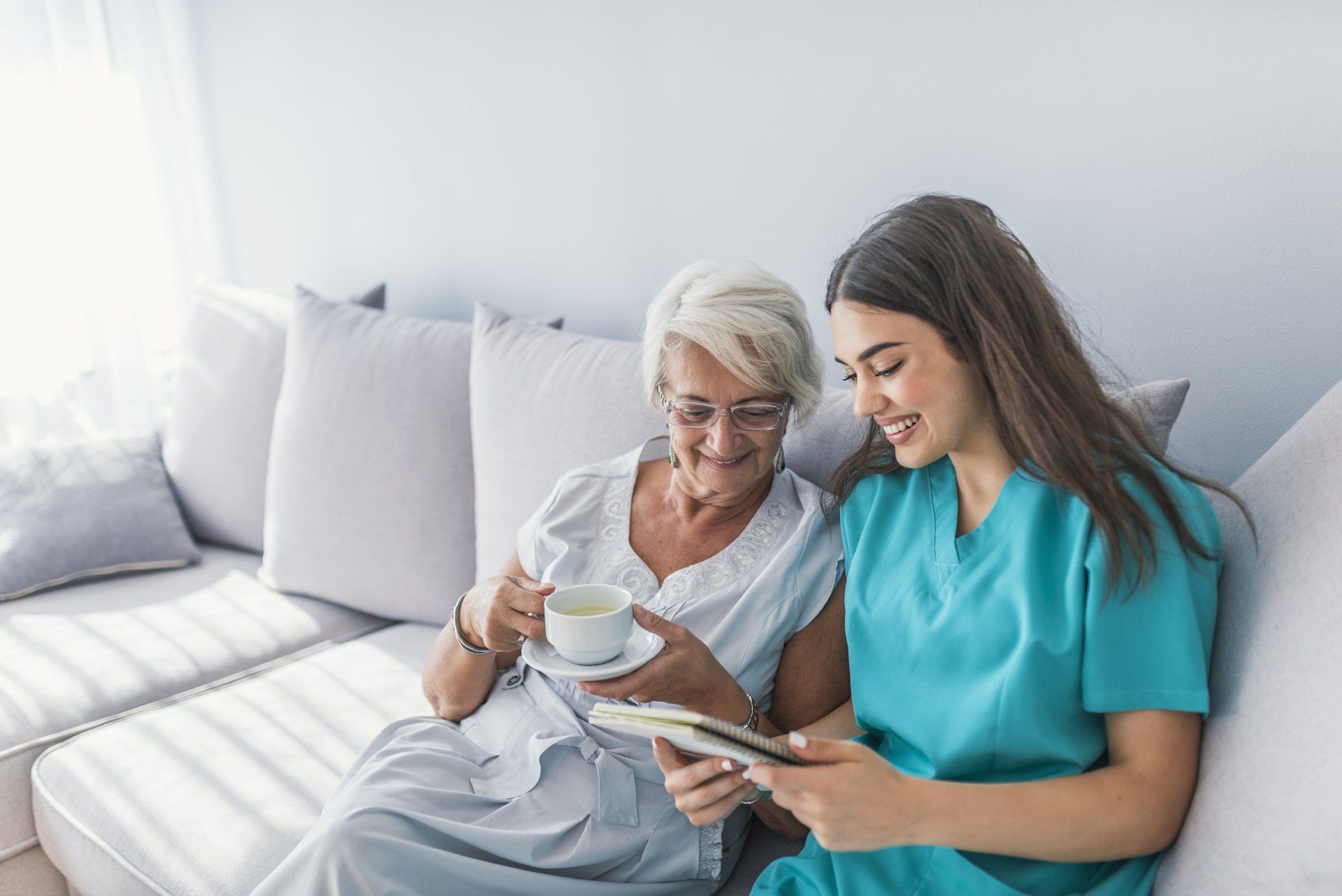 elderly woman and companion sitting on couch reviewing a notebook together