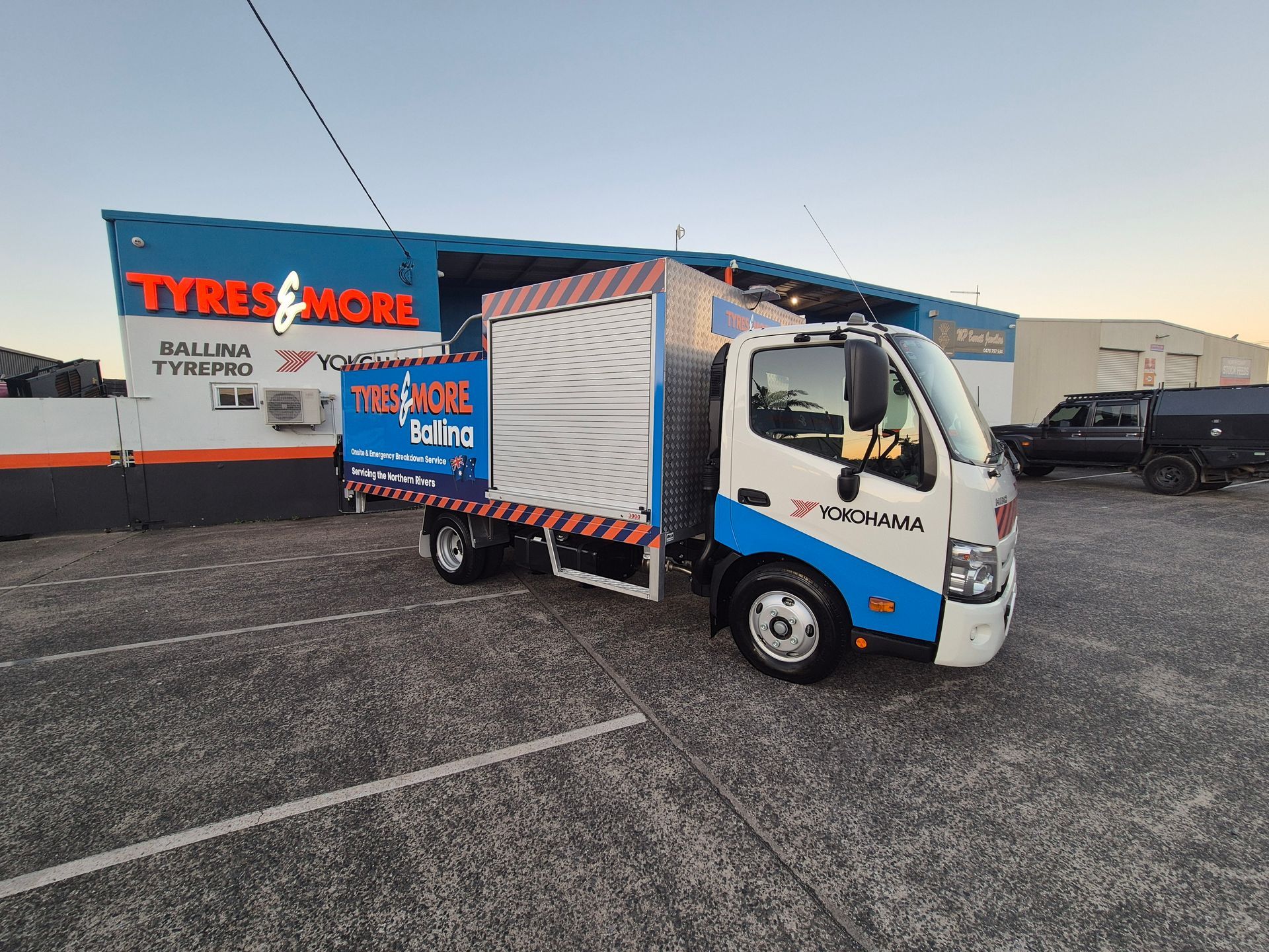 Blue and white delivery truck parked outside a Tyres & More store in a gravel lot at sunset — Ballina Tyrepro in Ballina, NSW
