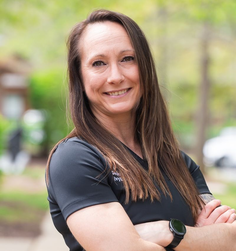 Smiling woman in a black shirt standing outdoors with arms crossed in a blurred park setting