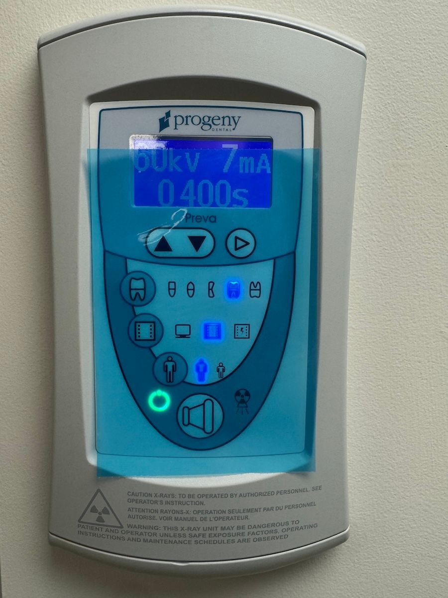 Blue medical device control panel with lit display and buttons on a gray wall-mounted unit