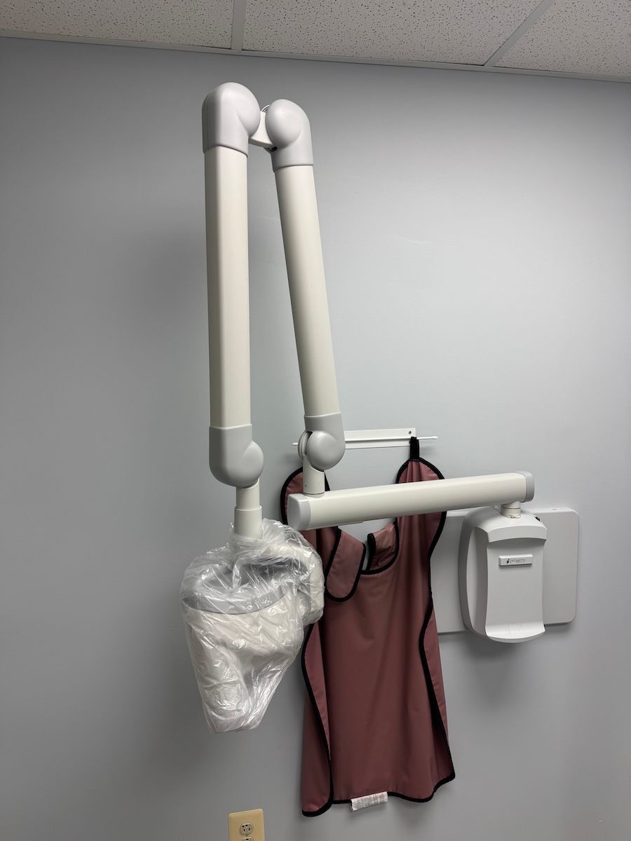 Wall-mounted hospital/surgical arm with a pink gown and plastic bag beneath it.