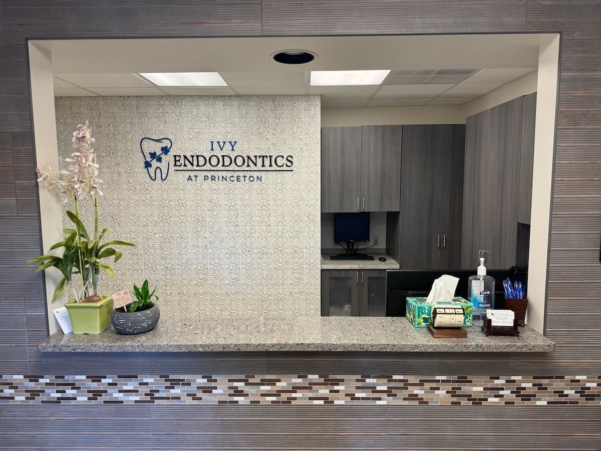 Dental office reception window with branded logo, countertop decor, and a dark computer monitor