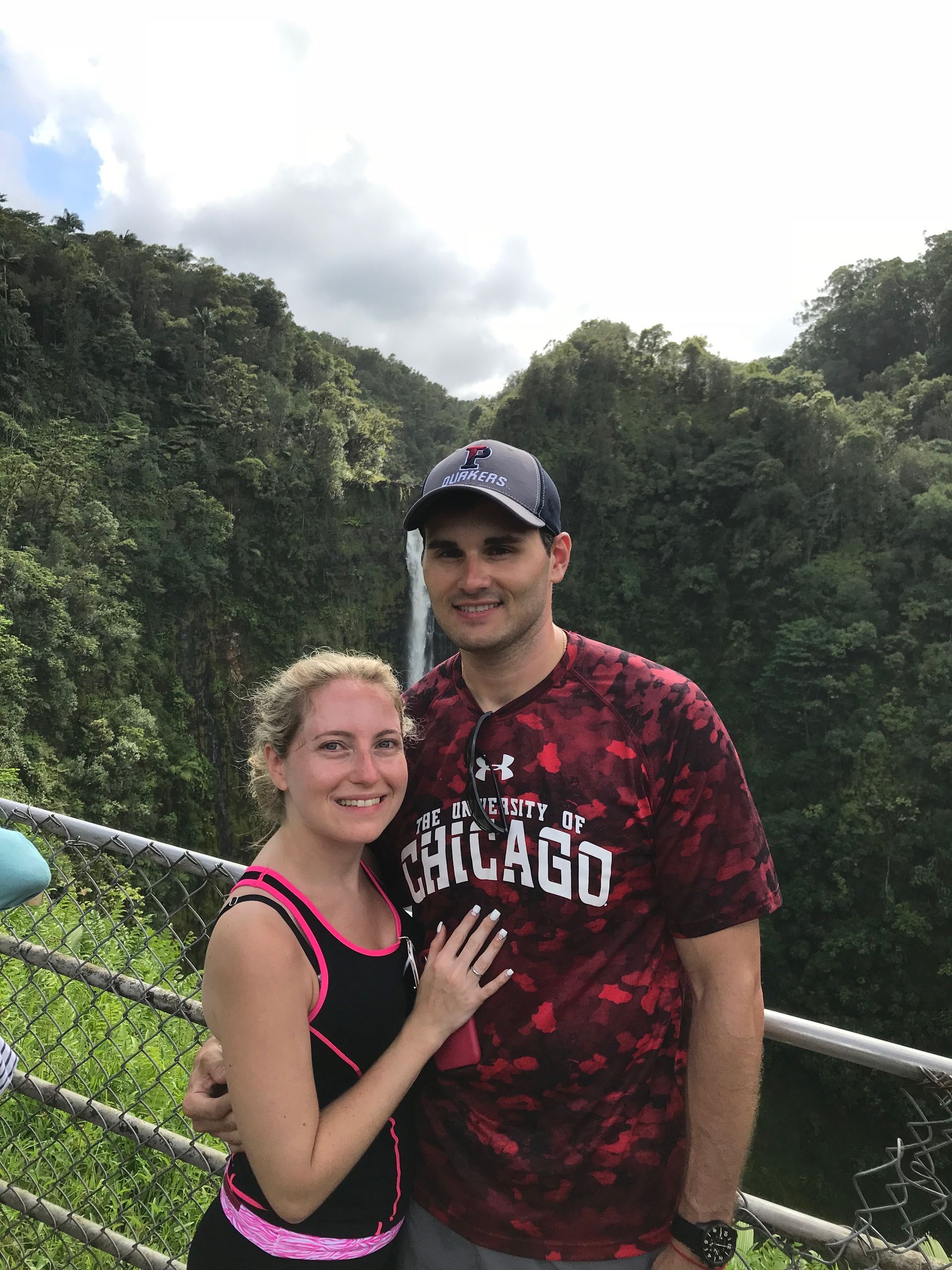 Two people smiling and posing by a railing with a lush green valley in the background.