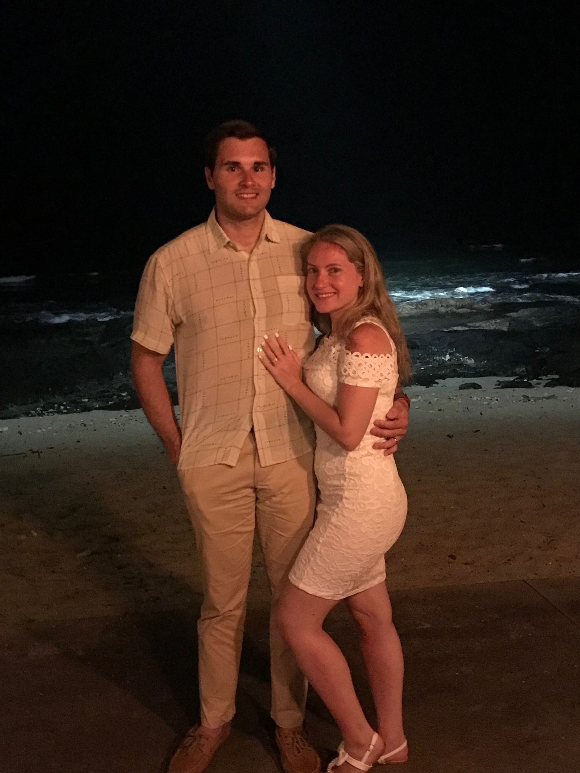 Couple standing on a beach at night, with waves in the background.