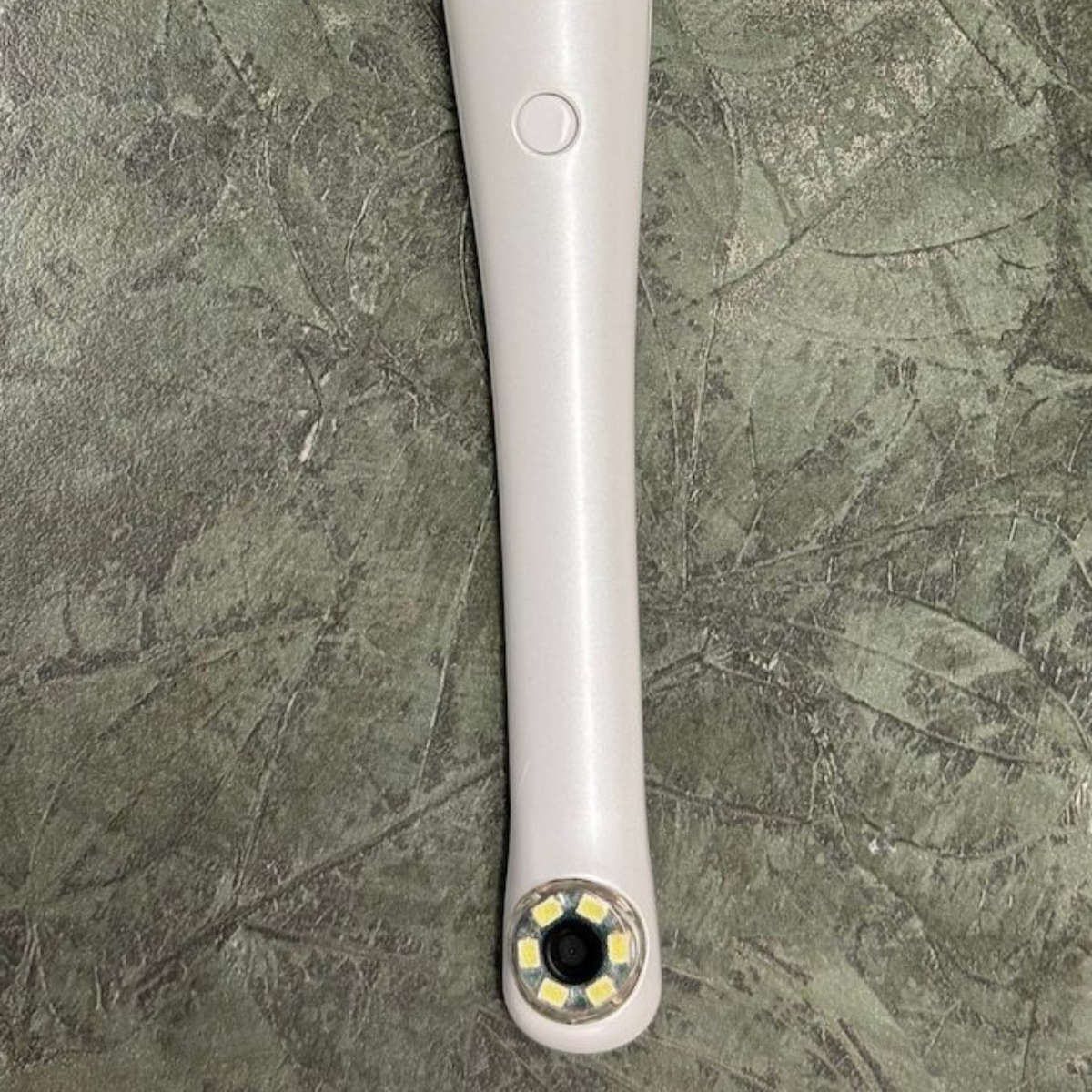 White electric toothbrush handle on a gray stone surface, with a circular power button and brush head end visible