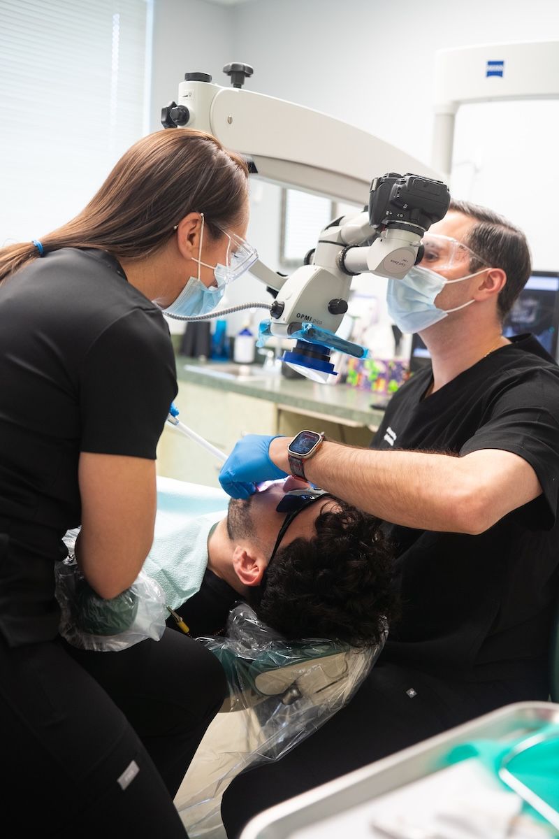 Dentist examining patient with a microscope while an assistant leans over the chair in a clinical room