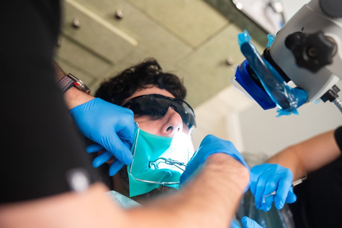 Dentists in blue gloves treating a patient wearing sunglasses and a face mask