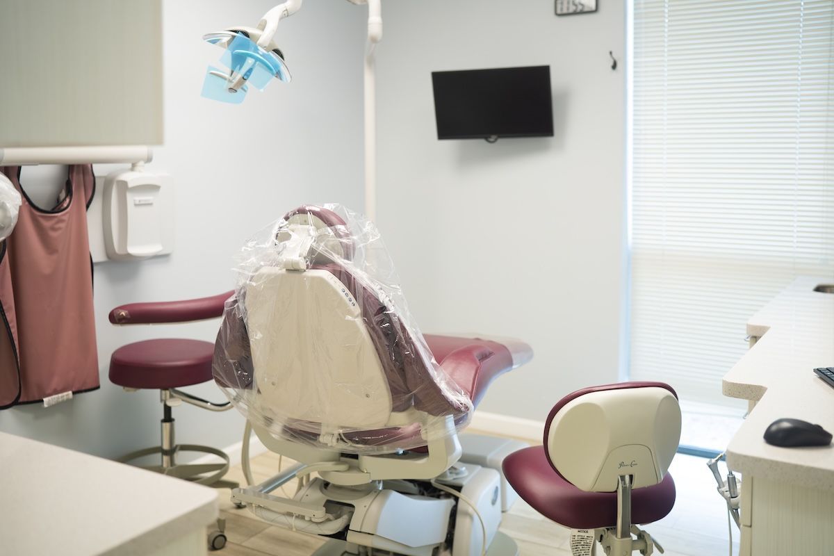 Empty dental exam room with chair, wall-mounted monitor, and bright window blinds
