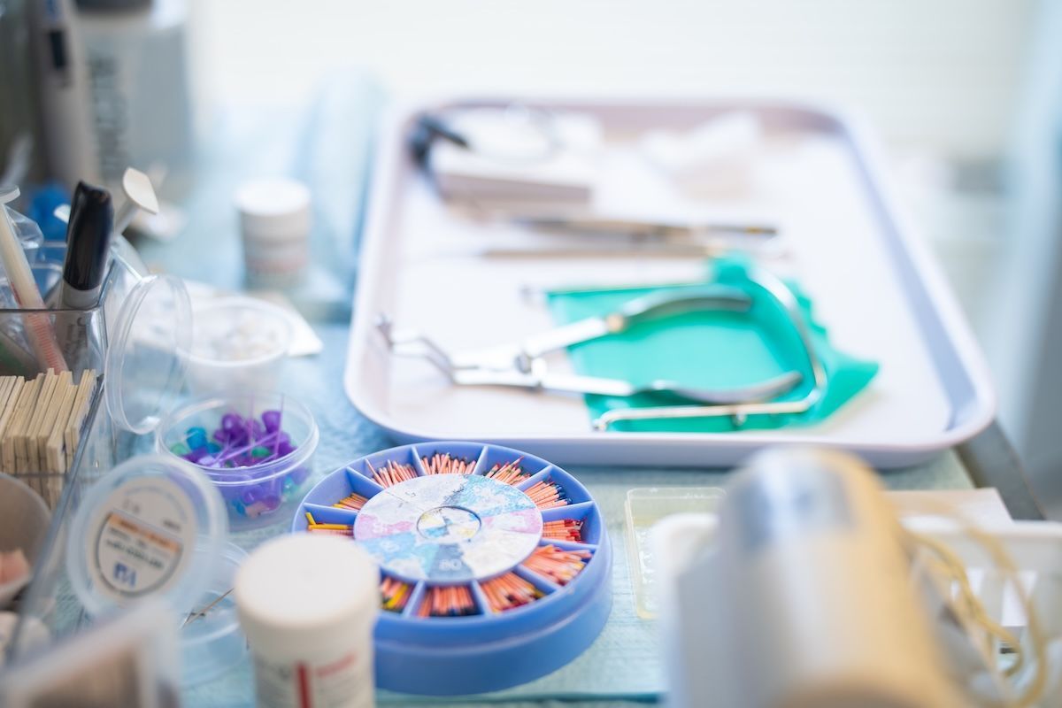 Dental instruments and supplies on a tray, including a blue tray, green tools, and a stopwatch