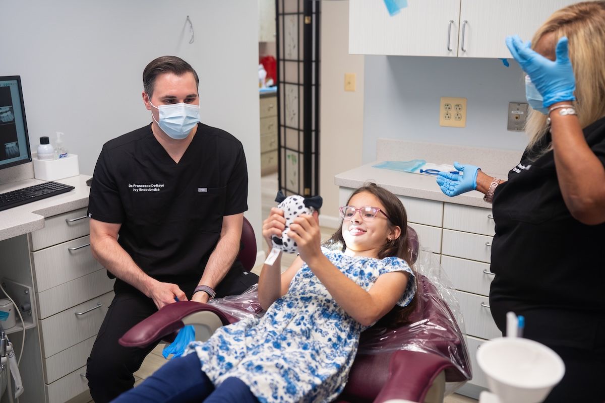 Dental patient in maroon chair smiling while clinician and assistant work in a clinic