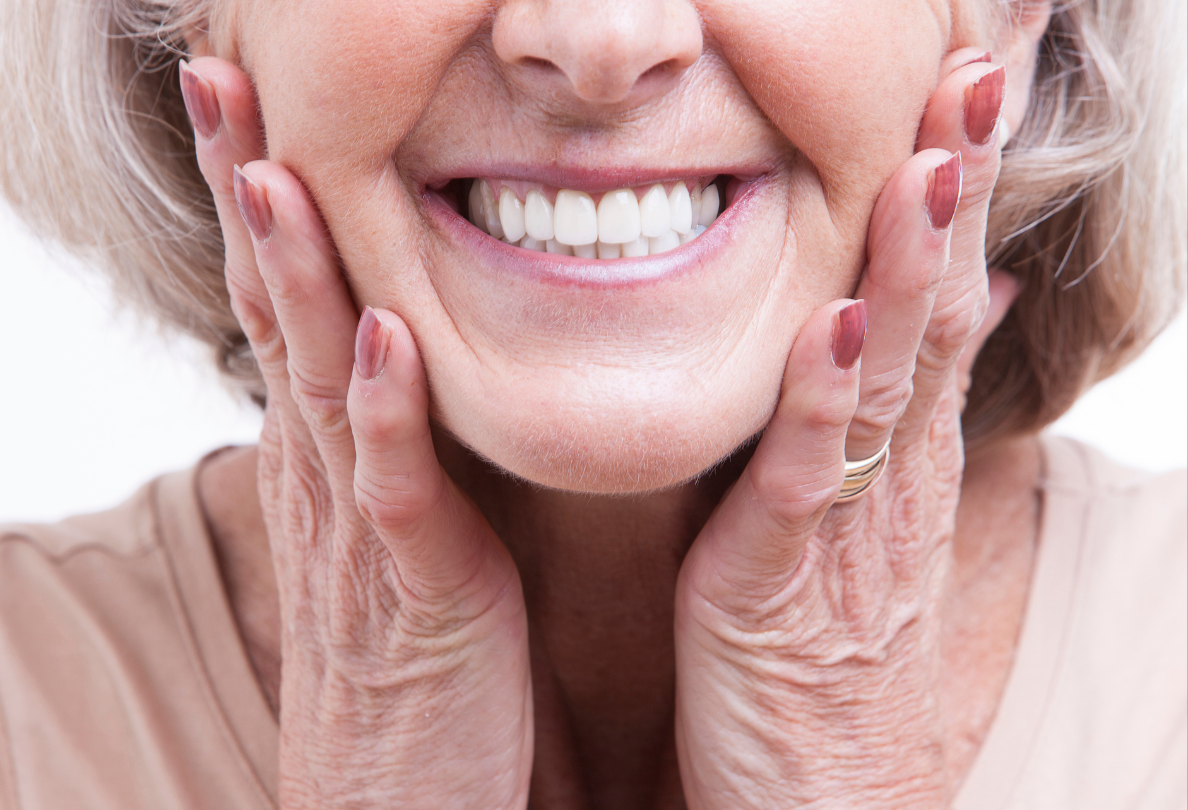 Smiling older woman with hands on face, showing white teeth.