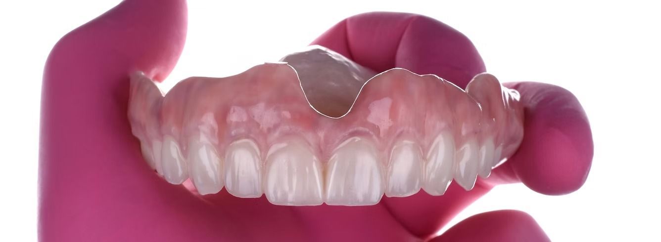 A set of dentures held in a pink gloved hand, isolated against a white background.