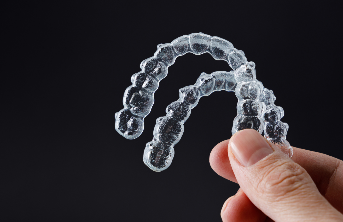 Hand holding clear aligners, dental braces, against a black background.