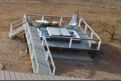 Elevated white platform with railings on a dry, sandy landscape, with stairs and rooftop equipment.