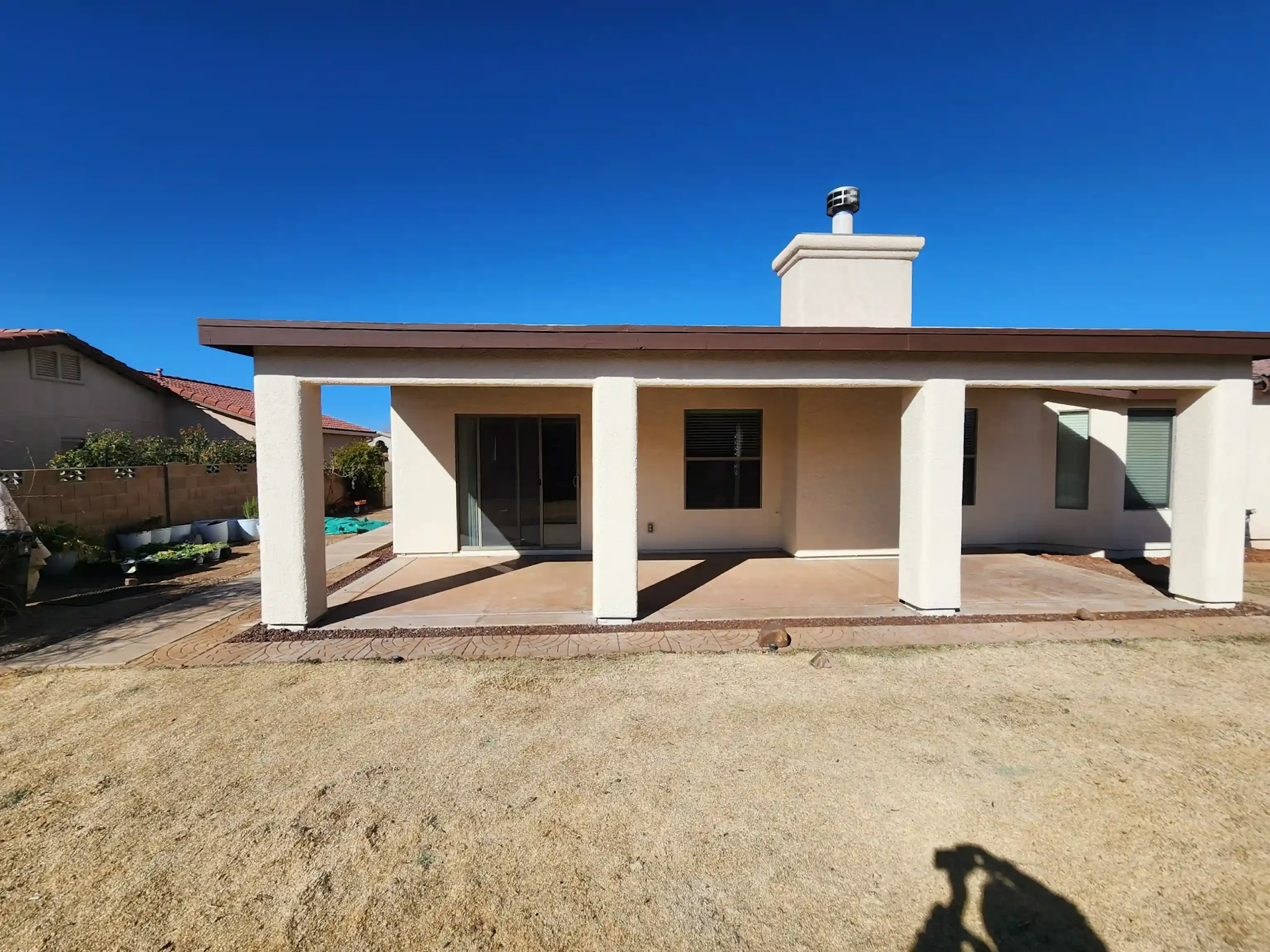 Single-story beige house with a covered patio and white columns under a clear blue sky.
