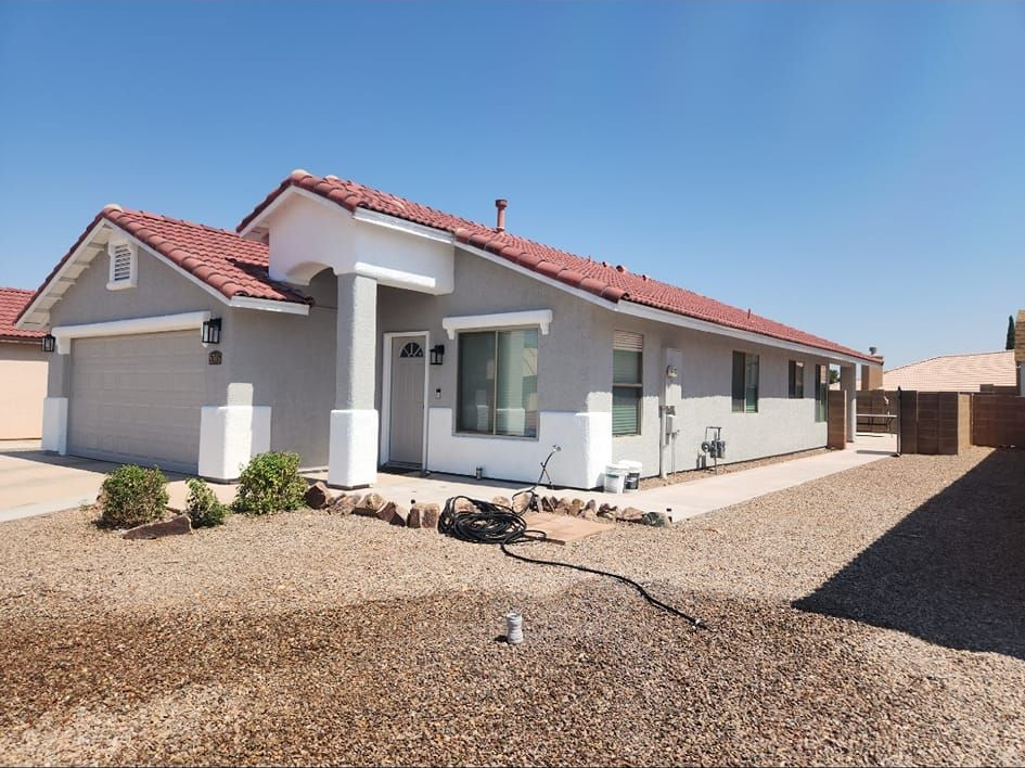 Single-story white house with red roof and gravel yard under a clear blue sky