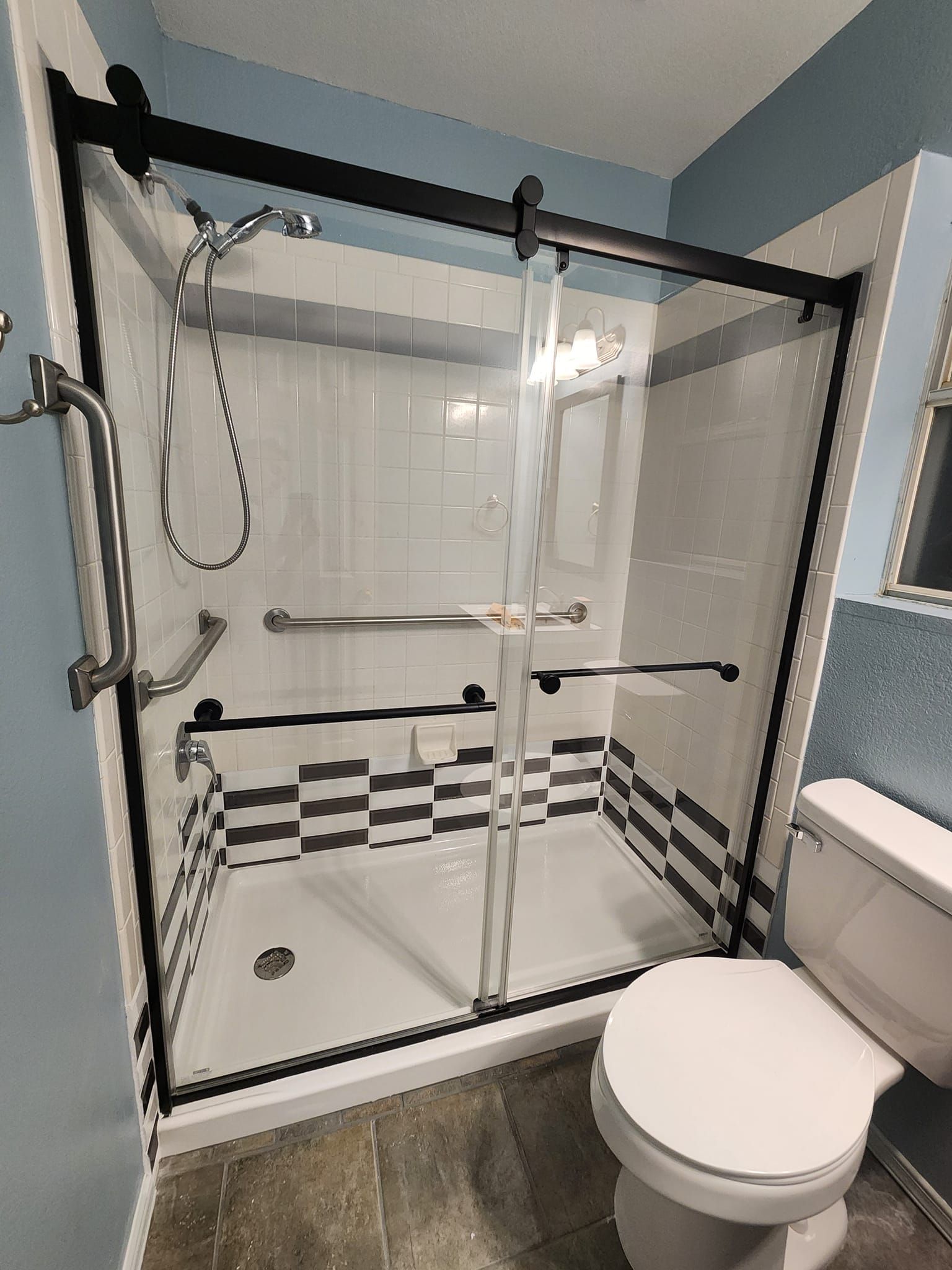 Bathroom with glass-enclosed walk-in shower, grab bars, fold-down seat, and toilet beside it
