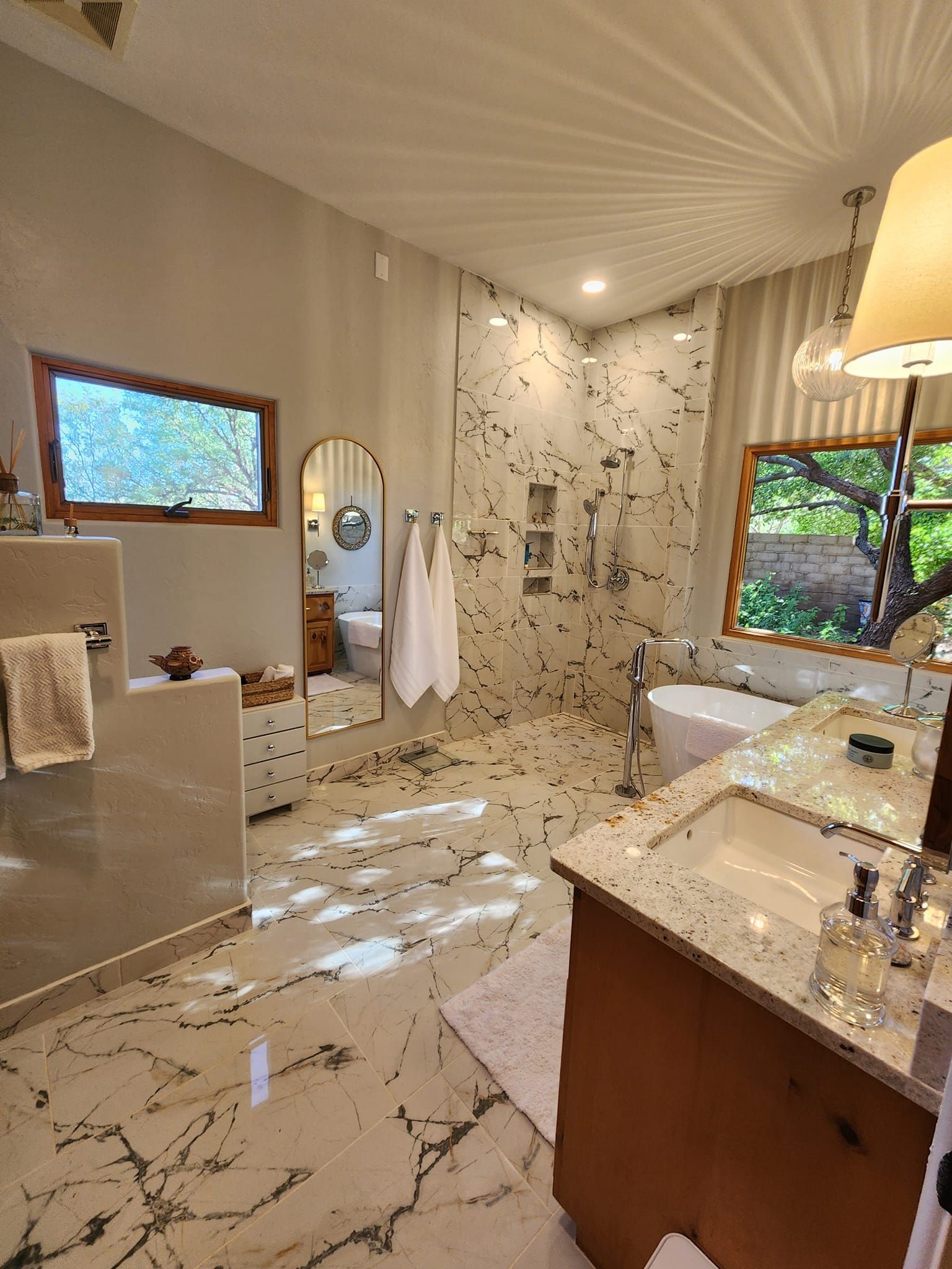Modern bathroom with marble floor, white walls, wooden vanity, walk-in shower, and large windows.