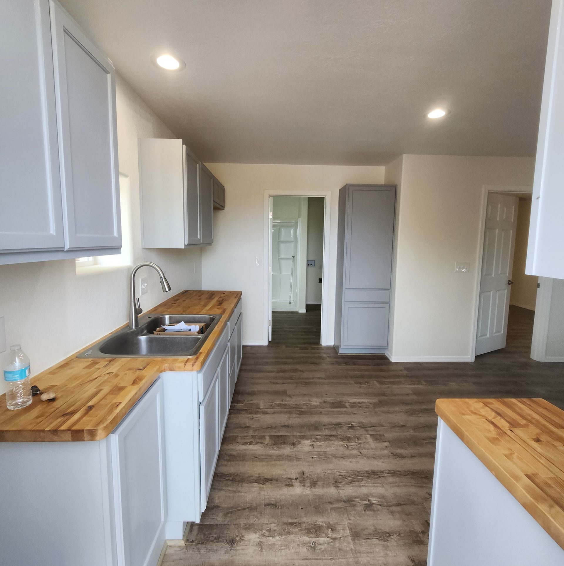 Modern kitchen with white cabinets, wood countertops, and dark wood flooring, viewed down a narrow galley.
