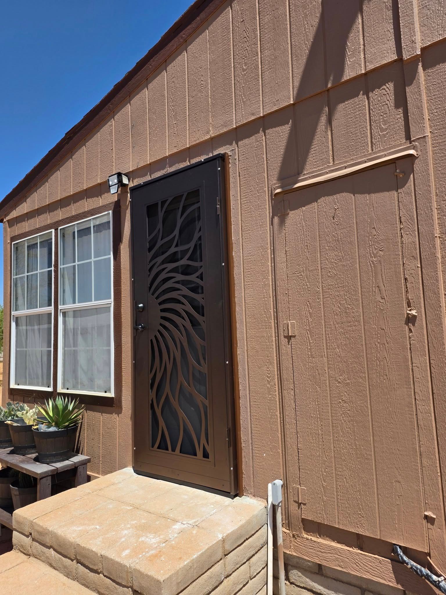 Exterior of a stucco house with a window, metal security door, and small front steps under a blue sky