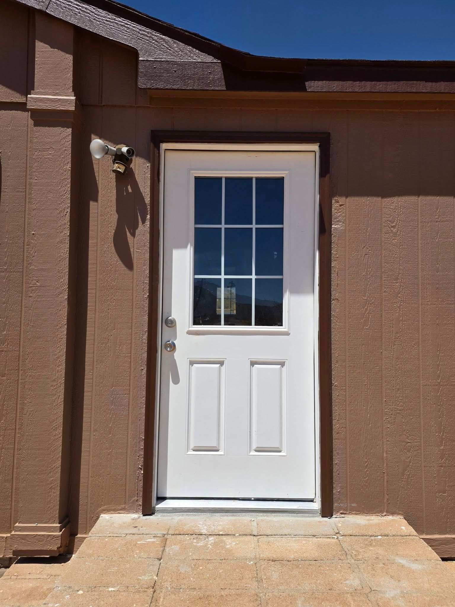 White door with window in tan stucco wall, beside a porch light and concrete step.