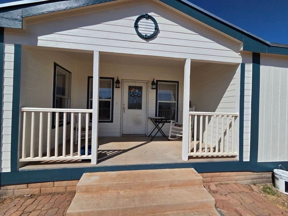 Front porch of a white house with blue trim, steps, railings, and a chair on the porch