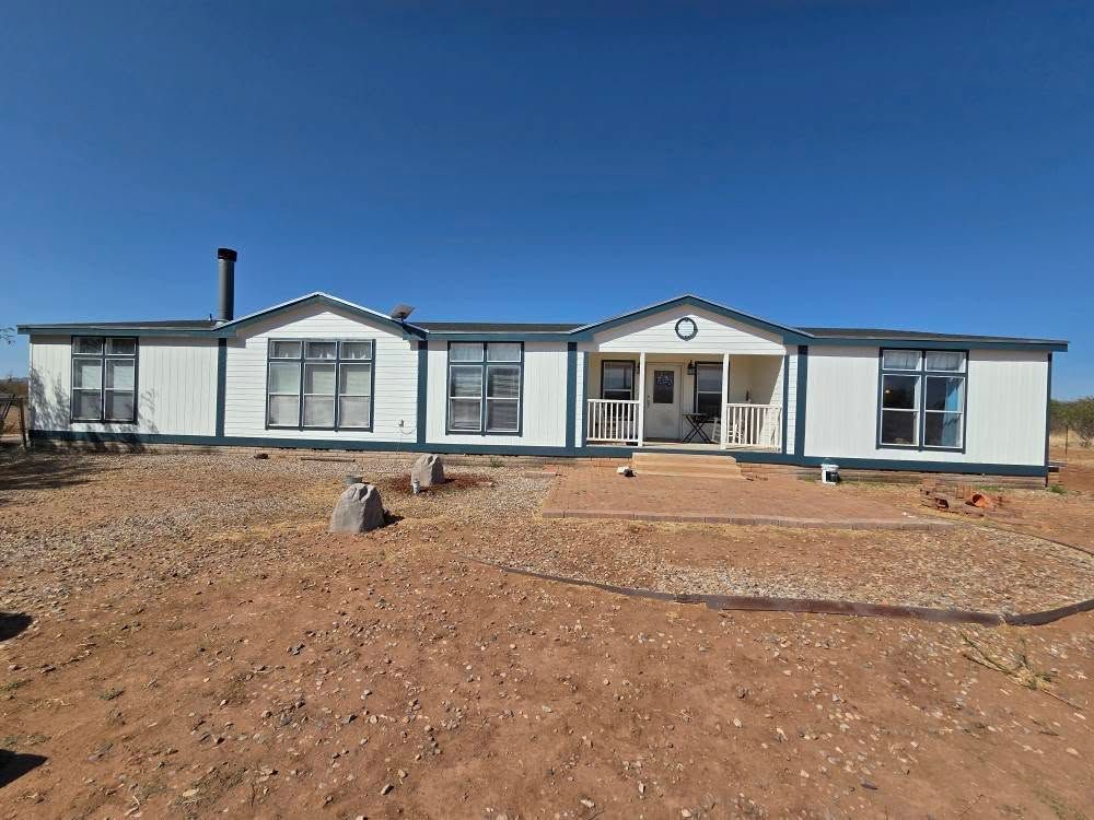 Single-story white house under a blue sky, with a wide dirt yard in front.
