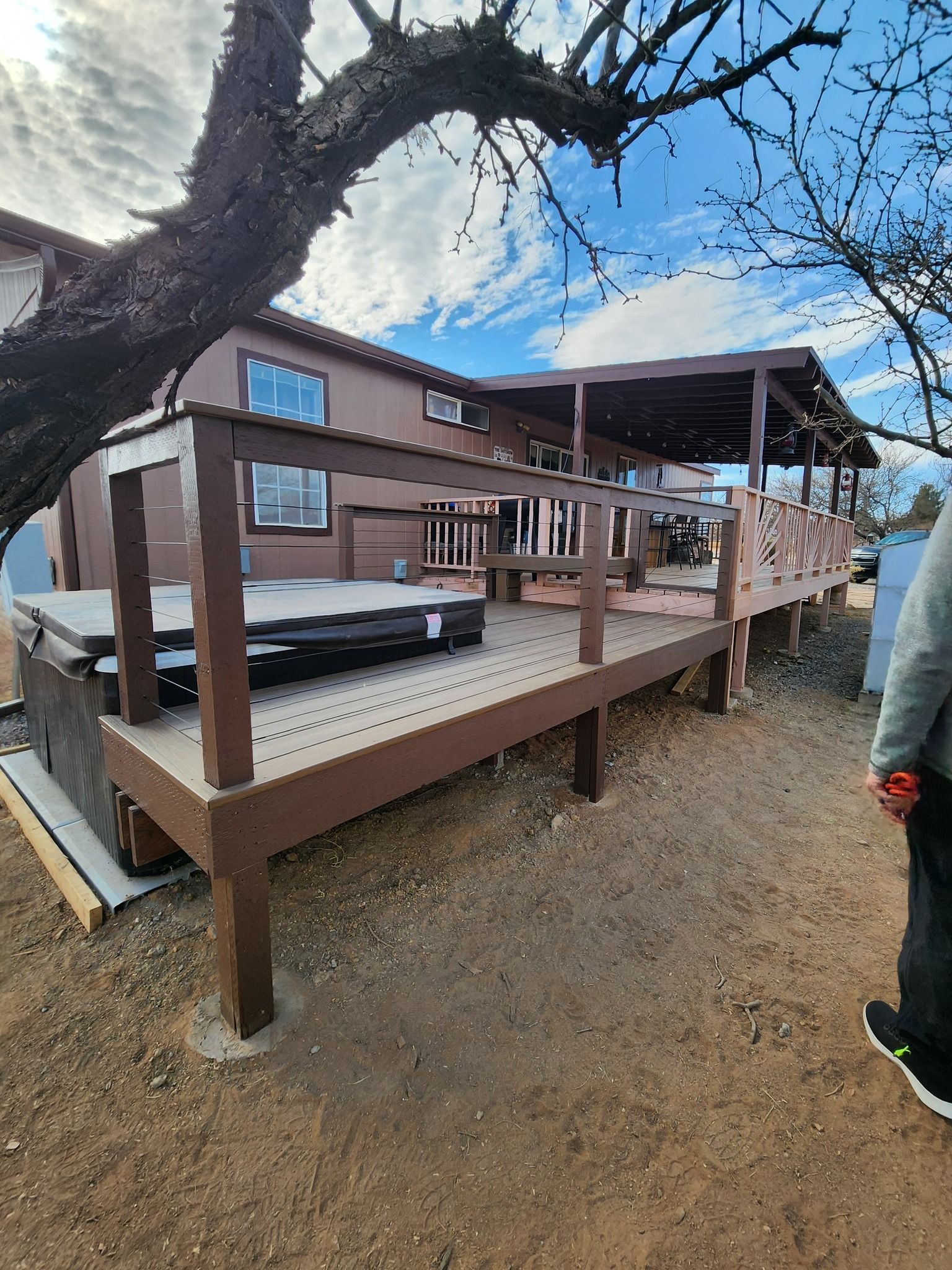 Wooden deck with stairs over a gravel yard beside a house under a clear blue sky