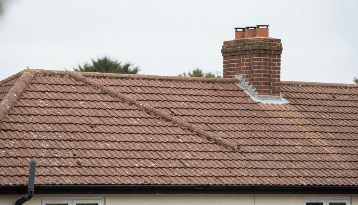 Brown tiled roof with a brick chimney and a small patch of damaged roofing.