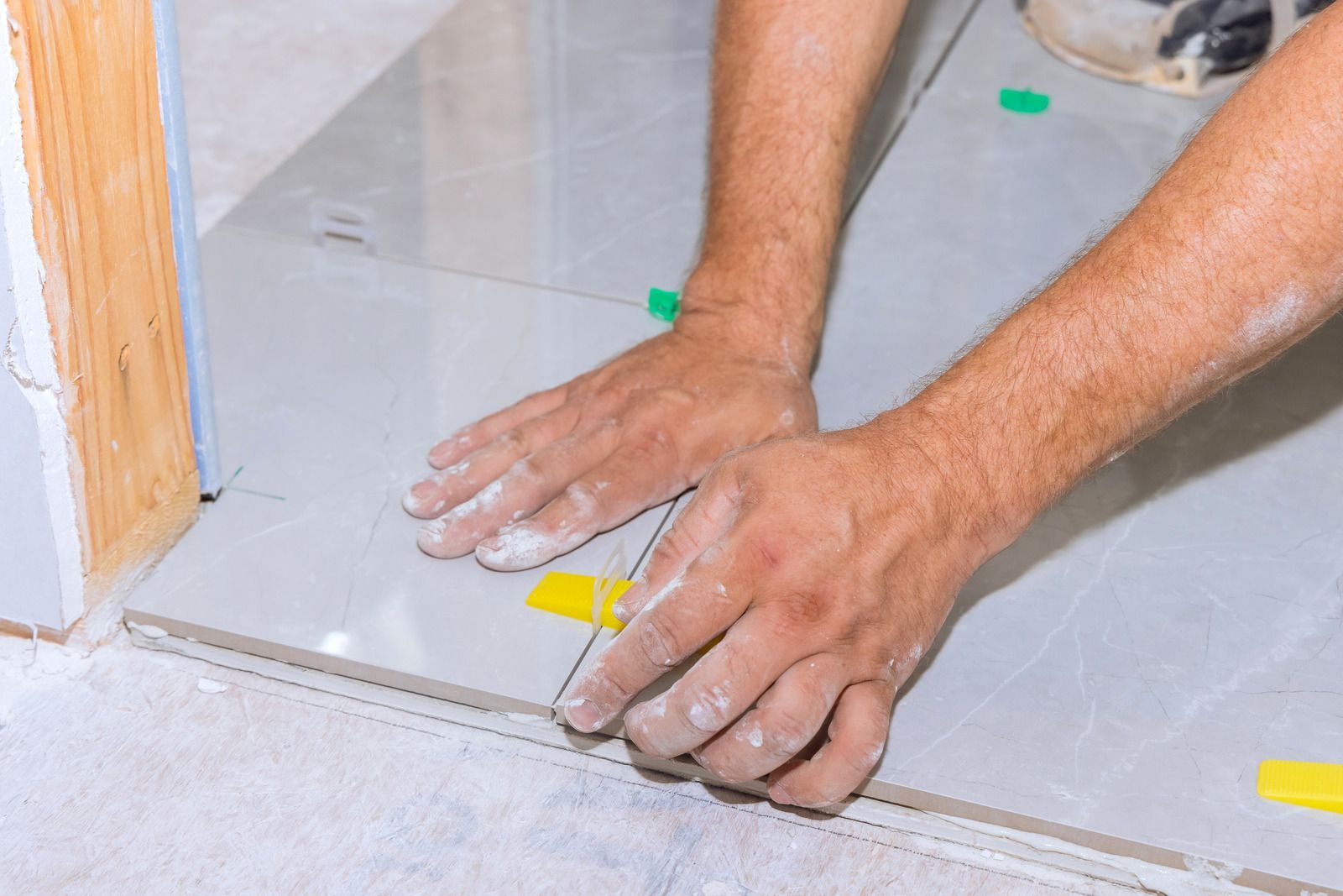 Hands aligning a yellow tile spacer on a tiled floor during installation work