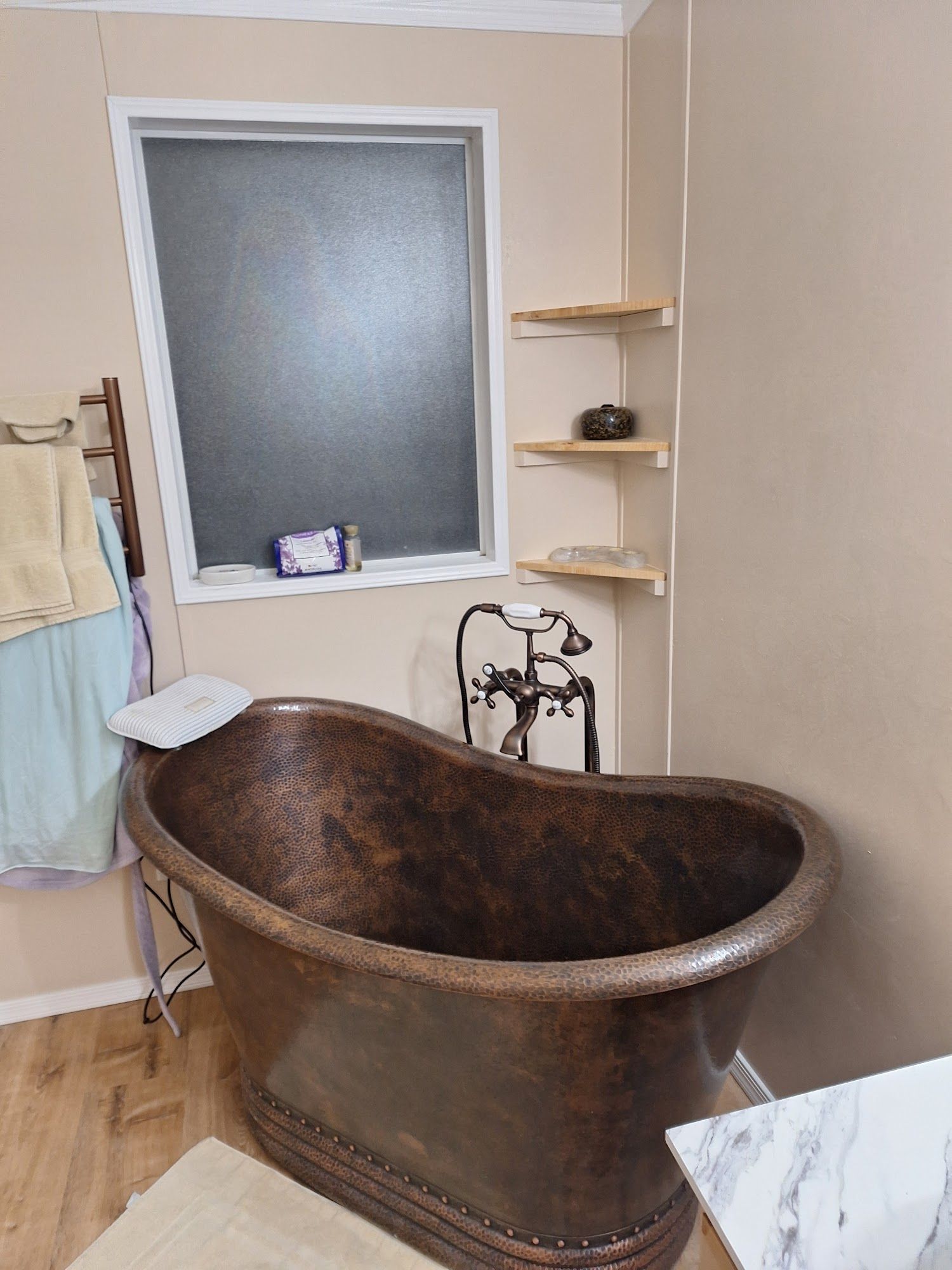 Rustic copper bathtub in a beige bathroom with frosted window and wall shelves