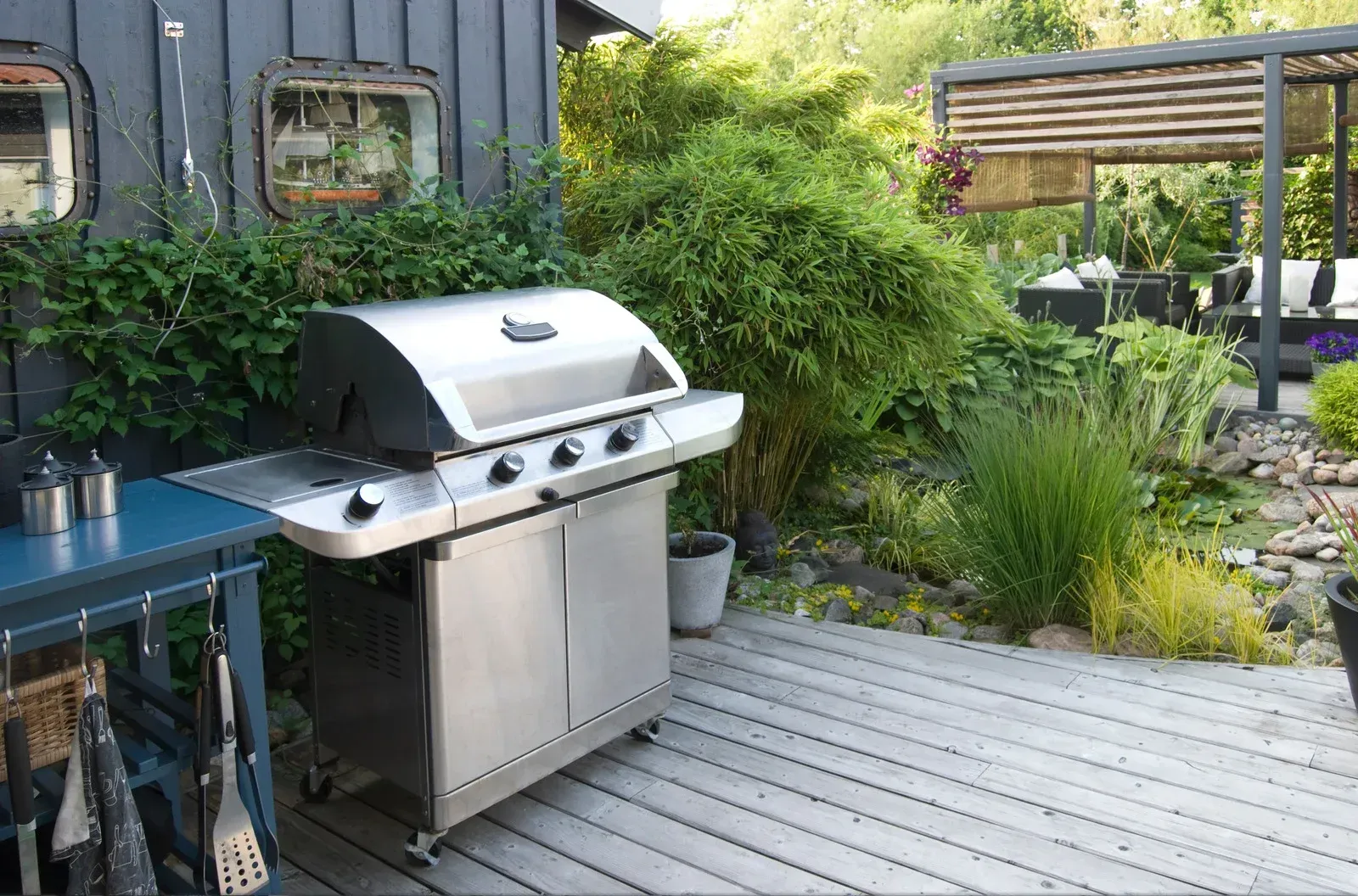 Stainless steel grill on a wooden deck beside lush green plants and a patio seating area
