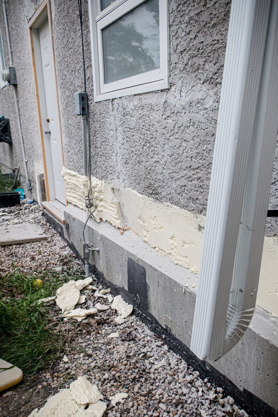 Worker scraping debris from the base of a white exterior wall during repair work