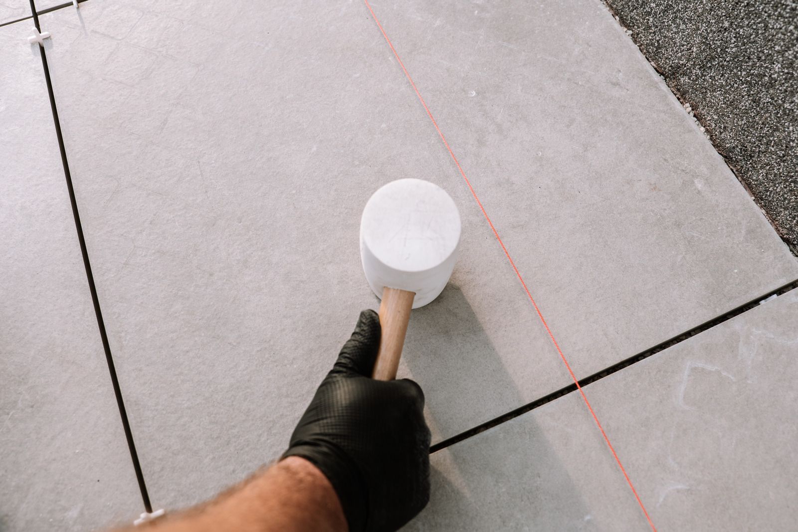 Gloved hand using a white mallet on gray concrete tiles with red chalk guide lines