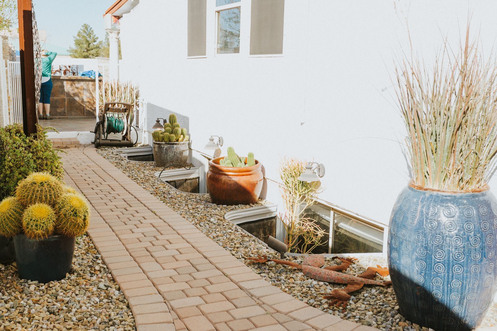 Gray small house with three small windows, a cactus by the wall, and a gravel yard under a clear blue sky