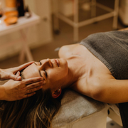 Woman receiving a facial massage on a spa table, covered with a towel.